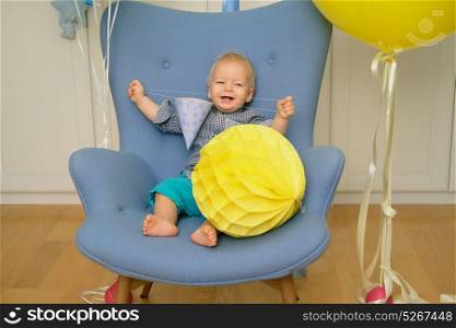 One year old baby boy first birthday. Toddler child sitting in chair and having fun with balloons