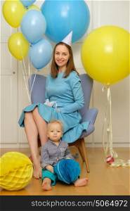 One year old baby boy first birthday. Toddler child with mother sitting in chair and having fun with balloons