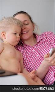One year old baby boy with his mother looking at smartphone screen. Indoor portrait