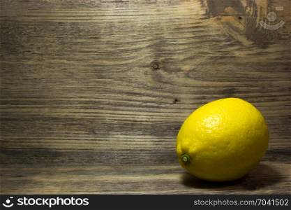 One yellow lemon on wooden background. Free space for text.