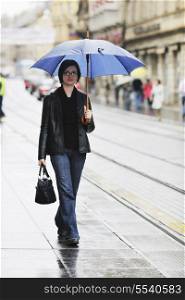 one young happy woman walking in cyti with rainy weater and blue umbrella