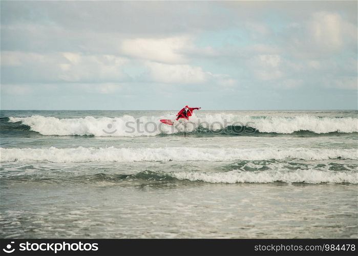 One young man surfer dressed as Santa Claus on the beach surfing