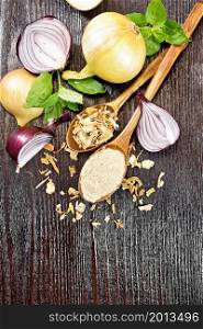 Onion powder and dried flakes in two spoons, purple and yellow onions, basil on wooden board background from above