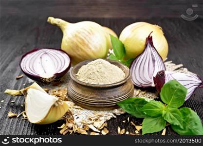 Onion powder in a bowl on a burlap napkin, purple and yellow onions, dried onion flakes and fresh basil on wooden board background