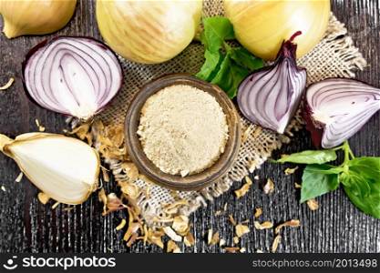 Onion powder in a bowl on burlap, purple and yellow onions, dried onion flakes and basil on wooden board background from above