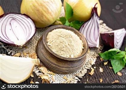 Onion powder in a bowl on burlap, purple and yellow onions, dried onion flakes and basil on dark wooden board background