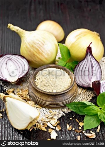Onion powder in a bowl on sacking, purple and yellow onions, dried onion flakes and fresh basil on wooden board background