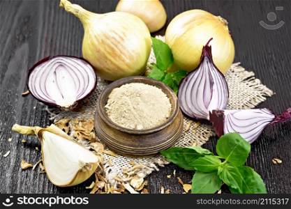 Onion powder in a bowl on sacking, purple and yellow onions, dried onion flakes and fresh basil on dark wooden board background