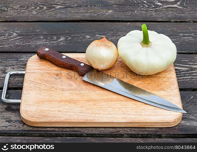 Onions, squash and knife on chopping board