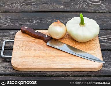 Onions, squash and knife on chopping board