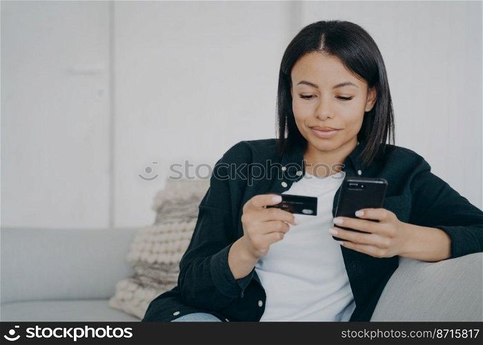 Online banking. Female holding credit card and smartphone, makes easy fast secure money transfer, using mobile bank app at home. Modern young woman makes purchases on internet, sitting on couch.. Online banking. Female holds credit card, phone, makes money transfer using mobile bank app at home