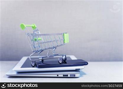 Online business and e-commerce or shopping online concept. Shopp. Online business and e-commerce or shopping online concept. Shopping basket on top of stack of laptop, tablet and mobile phone. Wireless technology for business with free copy space.
