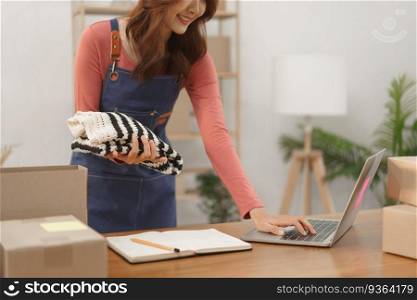 Online business merchant concept, Women entrepreneur checks order on laptop and pack clothes in box.