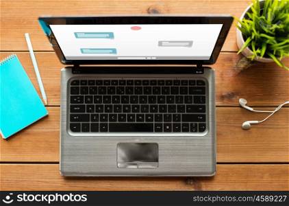online communication, education, business and technology concept - close up of laptop computer with messenger or internet chat on screen on wooden table