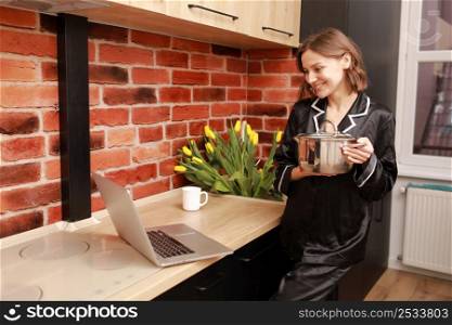 Online cooking tutorial. cropped photo hand of woman girl using laptop for vlogging blogging holding saucepan in the modern kitchen.. Online cooking tutorial. cropped photo hand of woman girl using laptop for vlogging blogging holding saucepan in the modern kitchen