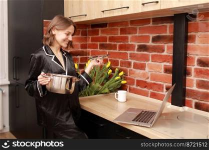 Online cooking tutorial. cropped photo hand of woman girl using laptop for vlogging blogging holding saucepan in the modern kitchen.. Online cooking tutorial. cropped photo hand of woman girl using laptop for vlogging blogging holding saucepan in the modern kitchen