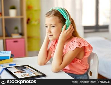 online education, e-learning and technology concept - happy student girl in headphones with teacher on tablet computer screen having video class at home. girl with tablet pc having online class at home