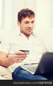 online or internet shopping concept - smiling man with laptop and credit card at home