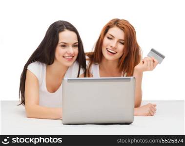 online shopping and technology concept - two smiling teenage girls with laptop computer and credit card