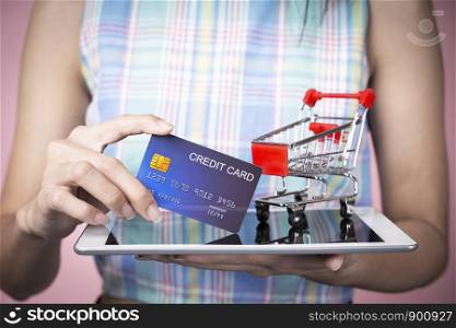 Online shopping concept. Closeup of hand holding credit card with cart on tablet screen.