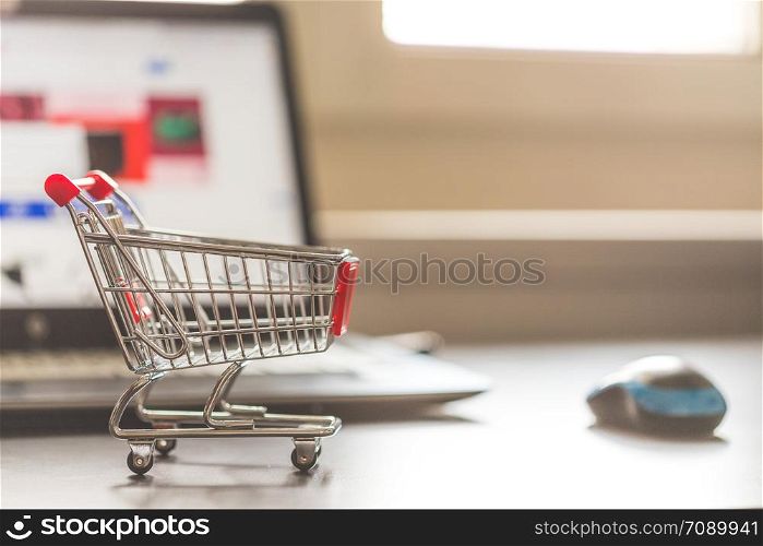 Online-Shopping concept: Miniature shopping cart, laptop and mouse in the blurry background
