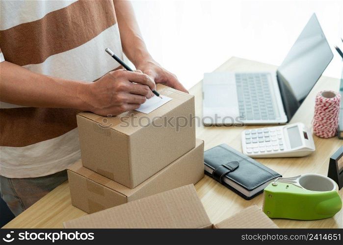 Online shopping concept the seller writing his customer’s address on the parcel and being ready for sending it.