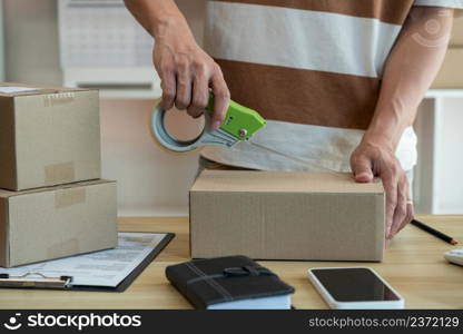 Online shopping concept the shop seller sealing the parcel of his goods on the desk.