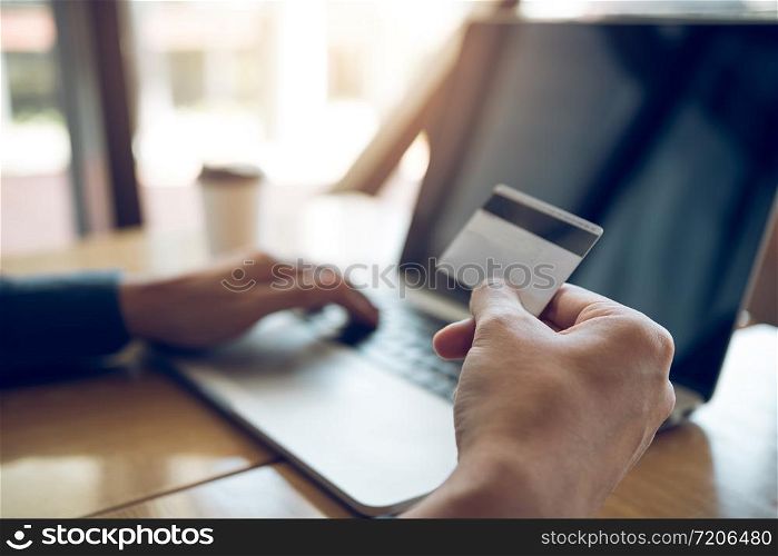 Online shopping concept with man hand using laptop and looking credit card for purchase order product.