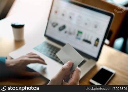 Online shopping concept with man hand using laptop and looking credit card for purchase order product.