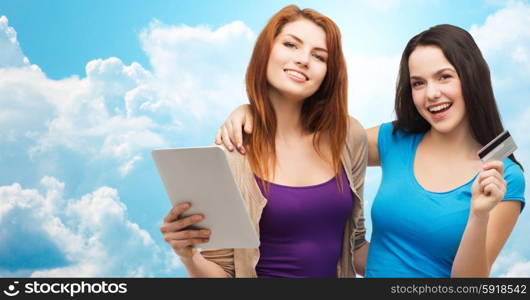 online shopping, e-money, commerce, people and technology concept - two smiling teenage girls or young women with tablet pc computer and credit card over blue sky with clouds background
