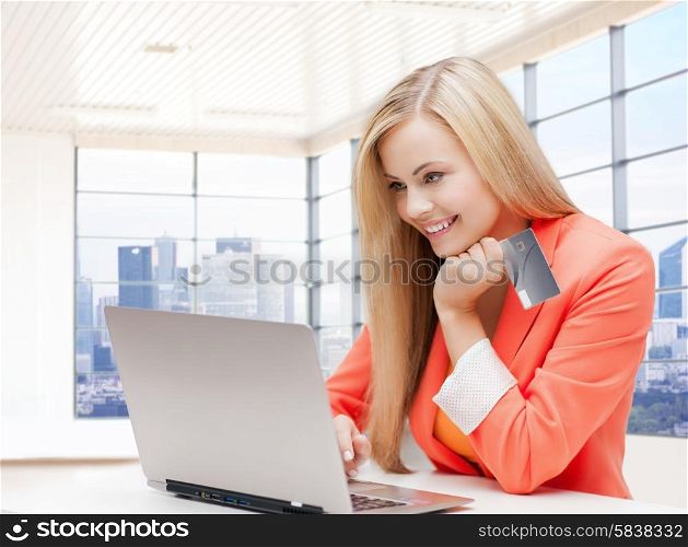 online shopping, people and technology concept - smiling young woman with laptop computer and credit card over office room background