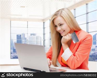 online shopping, people and technology concept - smiling young woman with laptop computer and credit card over office room background