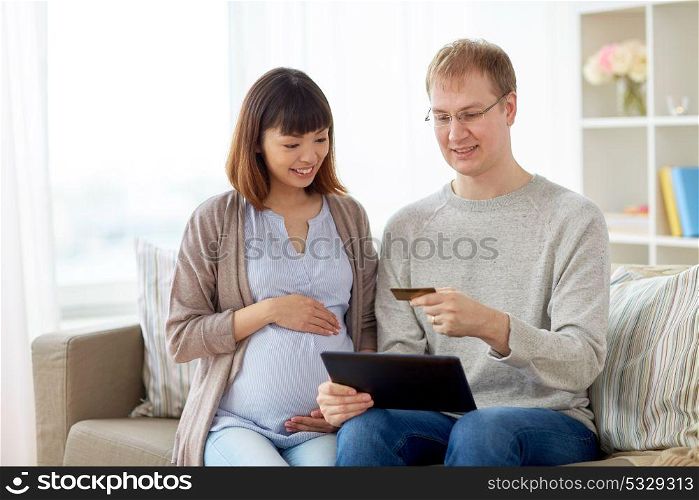online shopping, pregnancy and people concept - happy husband and his pregnant wife with tablet pc computer and credit card at home. husband and pregnant wife shopping online at home
