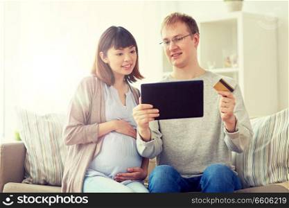 online shopping, pregnancy and people concept - happy husband and his pregnant wife with tablet pc computer and credit card at home. husband and pregnant wife shopping online at home