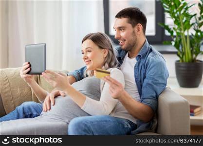 online shopping, pregnancy and technology concept - happy man and his pregnant wife with tablet pc computer and credit card at home. man and pregnant wife shopping online at home
