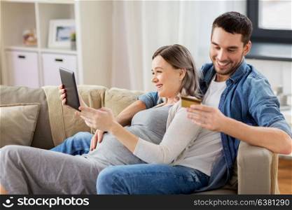 online shopping, pregnancy and technology concept - happy man and his pregnant wife with tablet pc computer and credit card at home. man and pregnant wife shopping online at home