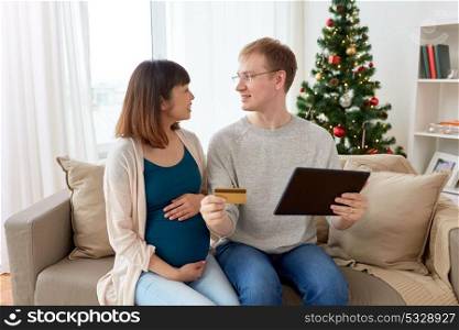 online shopping, winter holidays and people concept - happy man and his pregnant wife with tablet pc computer and credit card home at christmas. man and pregnant wife shopping online at christmas