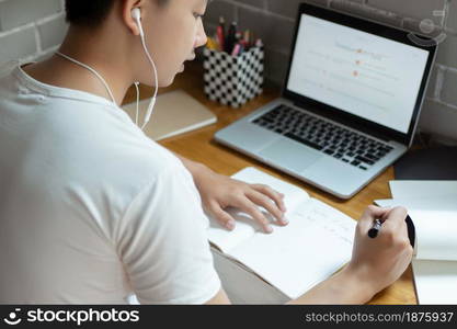 Online studying concept the high school student listening to music through his earphones and using his laptop to search information about his homework on the paper.