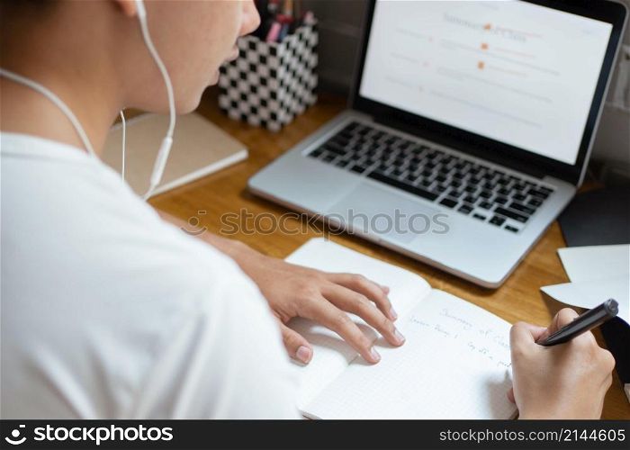 Online studying concept the high school student listening to music through his earphones and using his laptop to search information about his homework on the paper.