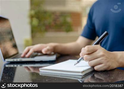 Online studying concept the man who is working from home attempting to write the meeting report down while online meeting of his company is conducting.