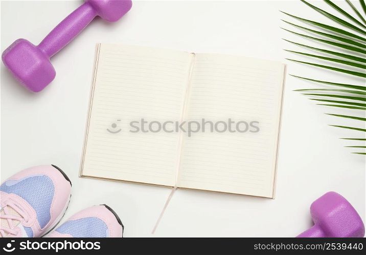 open blank notebook, a pair of sports gym shoes and dumbbells on a white background. Place for recording, top view
