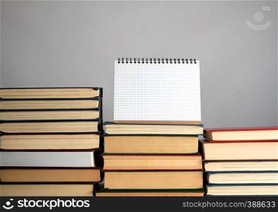 open blank notebook is standing on the stack of books, gray background
