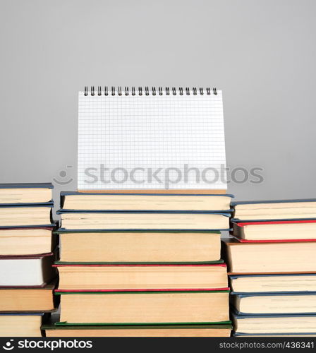 open blank notebook is standing on the stack of books, gray background