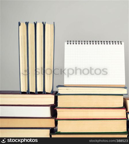 open blank notebook is standing on the stack of books, gray background, copy space