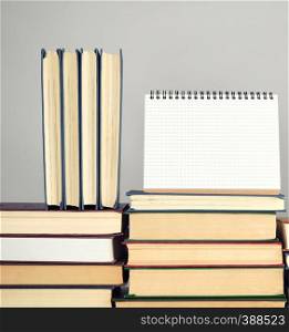 open blank notebook is standing on the stack of books, gray background, copy space
