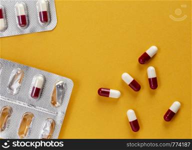 Open blister pack of tablets and a few red and white medicinal capsules with atybiotics on yellow background. Open blister pack of tablets and a few red and white medicinal capsules with atybiotics