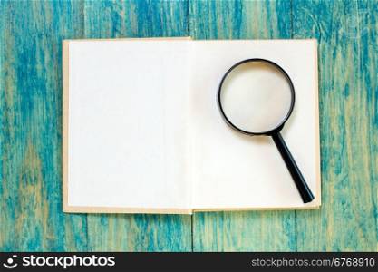 Open book and magnifier on blue wood surface