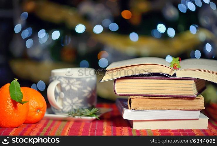 Open book, cup of hot drink and orange fruits with holidays background