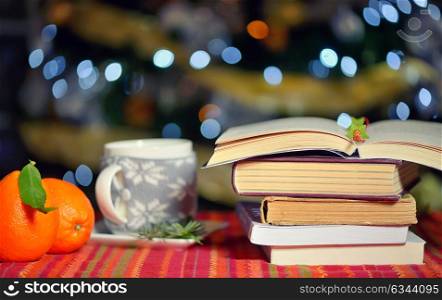 Open book, cup of hot drink and orange fruits with holidays background