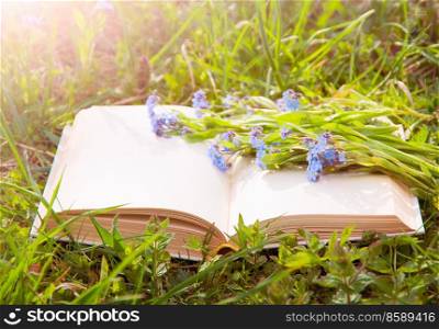 Open book on green grass with flowers close-up